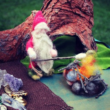 130925 Needle-felted Grumpy Red Gnome roasting marsh mellows over open kindling fire pit. Square cropped. 